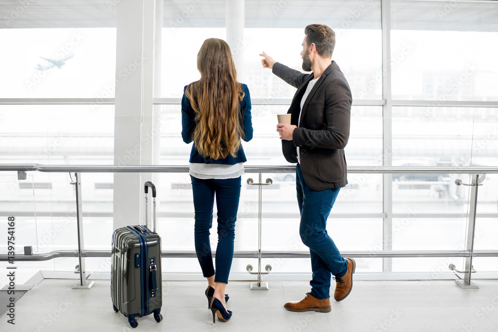 Business couple standing together with baggage near the window at the departure area at the airport