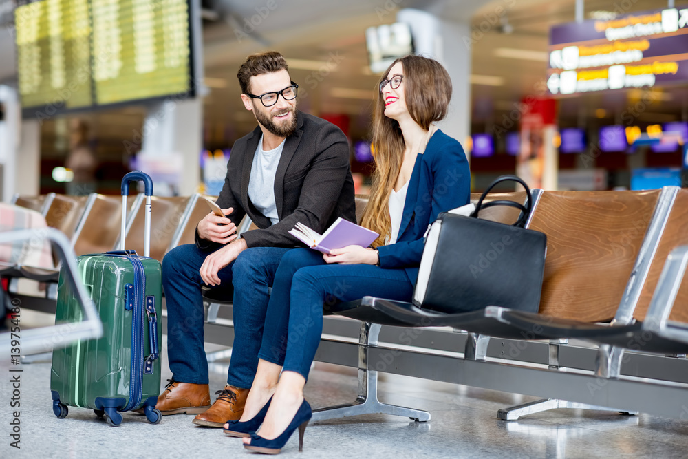 Elegant business couple sitting with phone and book at the waiting hall in the airport. Business tra