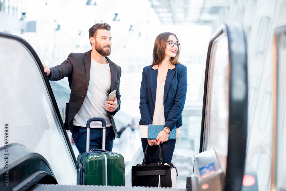 Elegant business couple with baggage getting up on the escalator to the departure area at the airpor