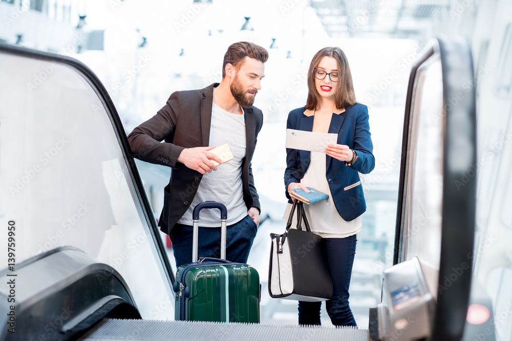 Elegant business couple with baggage getting up on the escalator to the departure area at the airpor