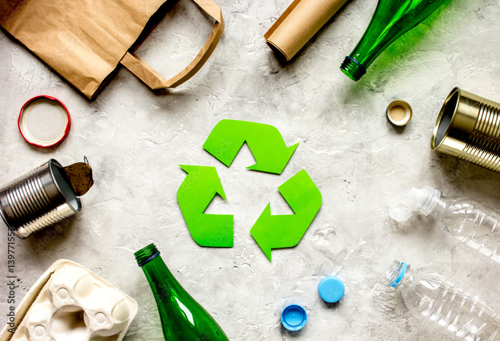 waste recycling symbol with garbage on stone background top view