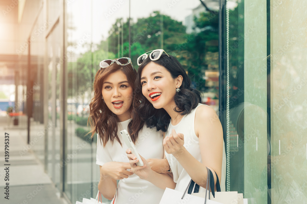 Beautiful asian girls with shopping bags using smartphone at the mall