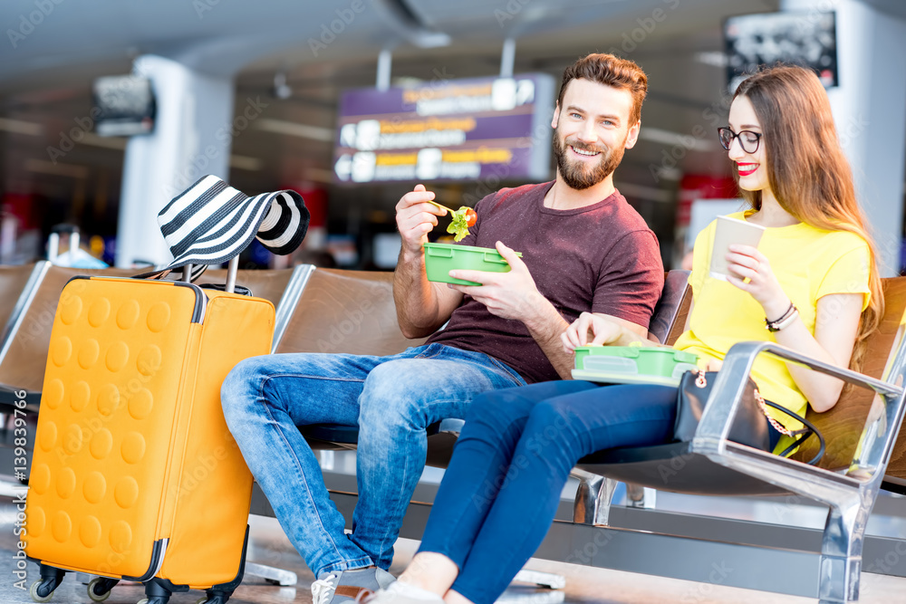 Young couple having a snack with lunch boxes at the waiting hall of the airport during their vacatio