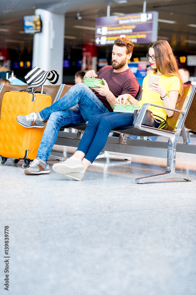 Young couple having a snack with lunch boxes at the waiting hall of the airport during their vacatio