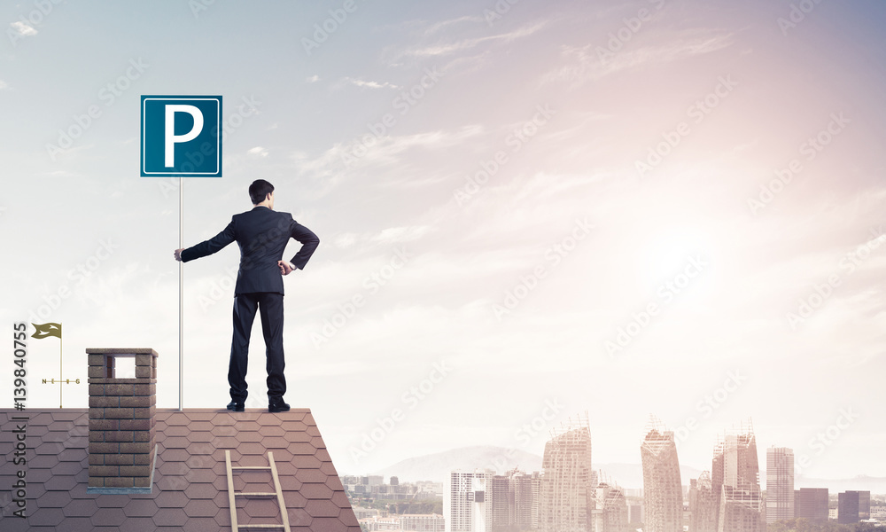 Young businessman with parking sign standing on brick roof. Mixe