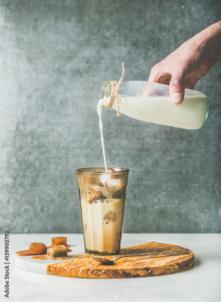 Mans hand pour milk to Iced焦糖拿铁咖啡鸡尾酒with冰冻咖啡冰块in glass