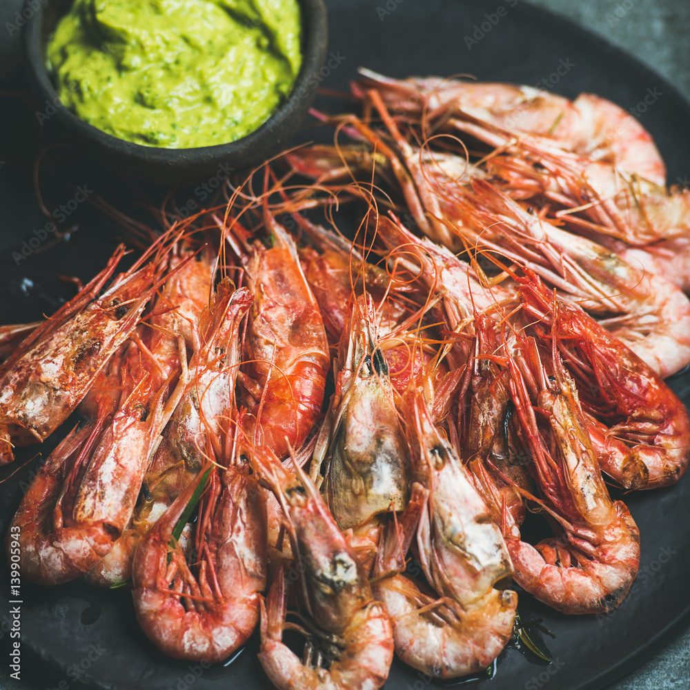 Roasted red shrimps with guacamole avocado sauce in slate stone black plate over grey concrete backg