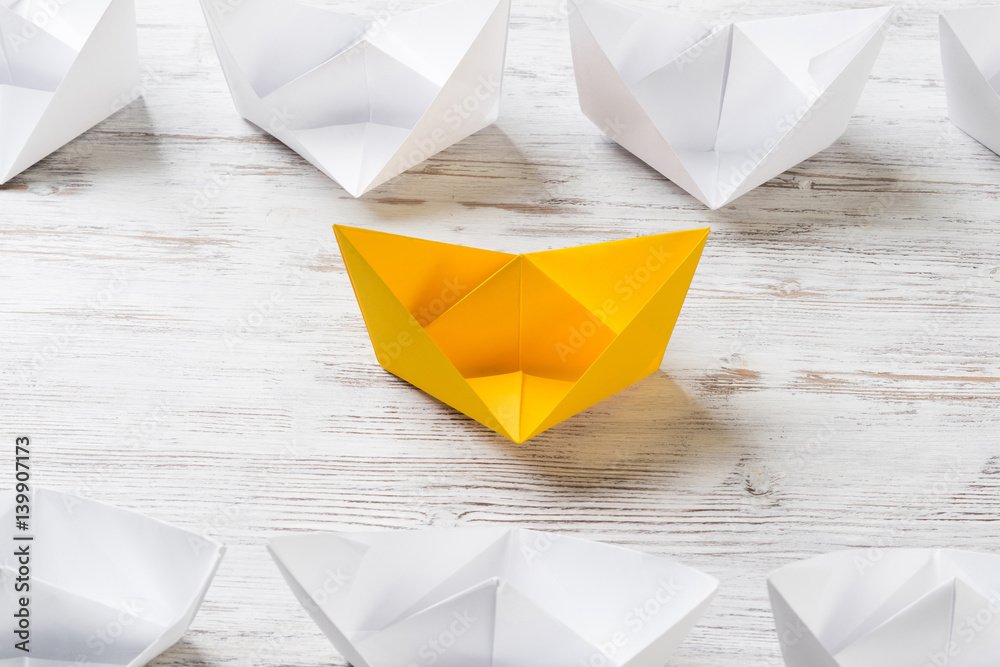 Business leadership concept with white and color paper boats on wooden table