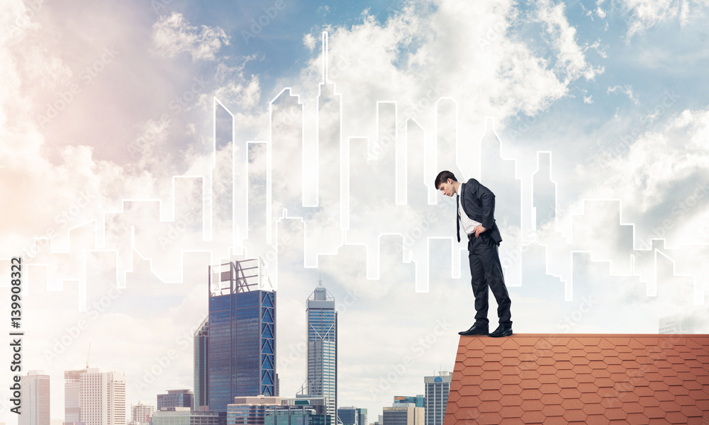 Businessman looking down from roof and modern cityscape at backg