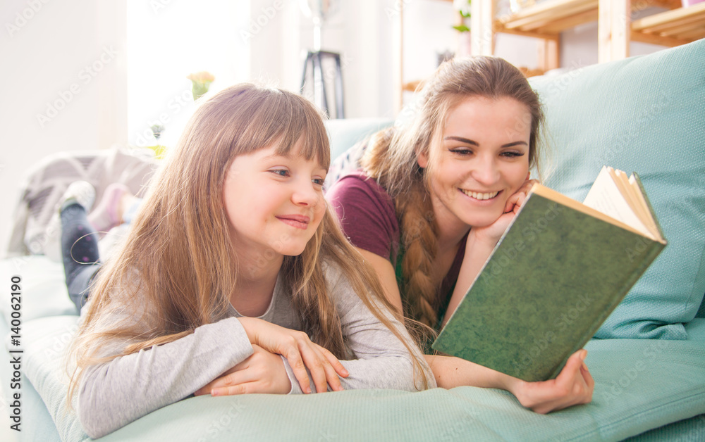 Mother and daughter sitting on sofa and reading book together