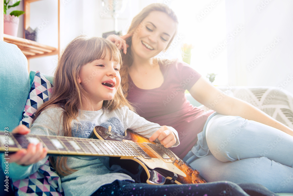 Mother and daughter at home, playing guitar and singing