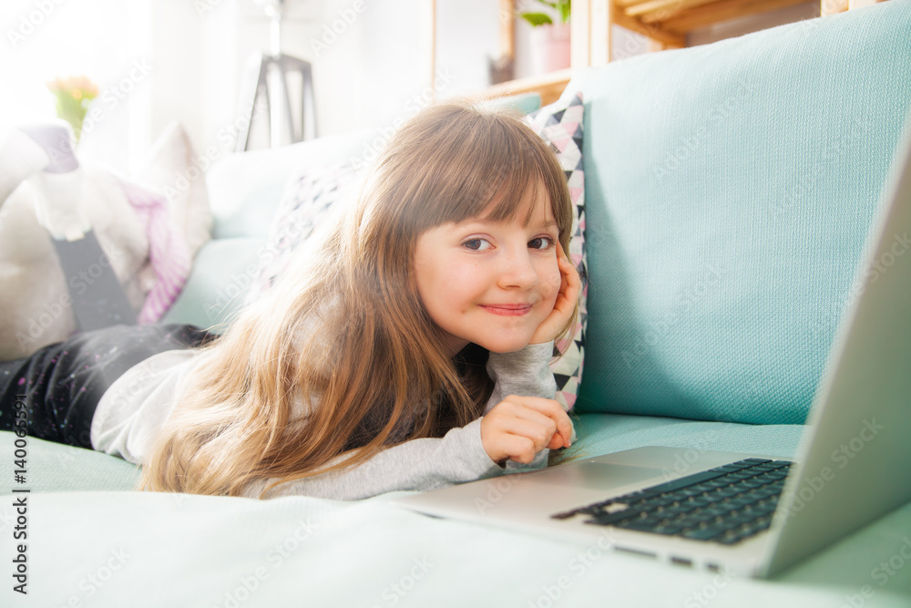 Cute little girl using laptop on sofa at home