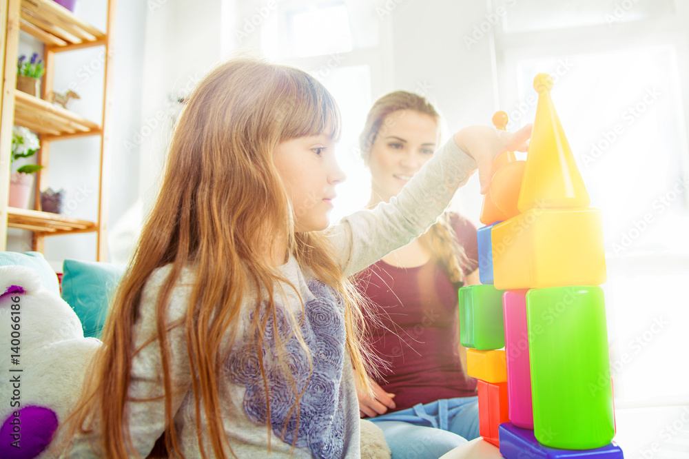 Cute little girl and her mother playing with blocks together, family at home