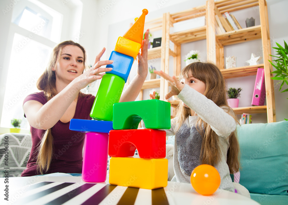 Cute little girl and her mother playing with blocks together, family at home