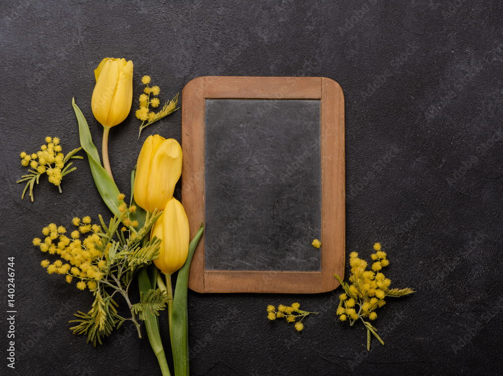 Yellow tulips with Mimosa on a black background and chalk board with copy space.