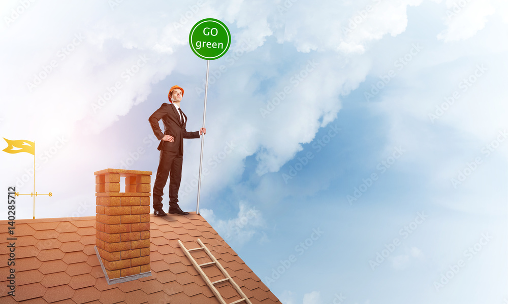 Businessman in suit on house top with ecology concept signboard. Mixed media