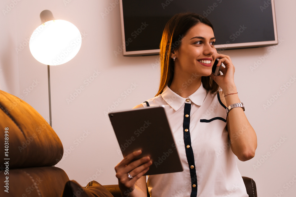 Happy young woman talking on the cell phone and using tablet computer at home