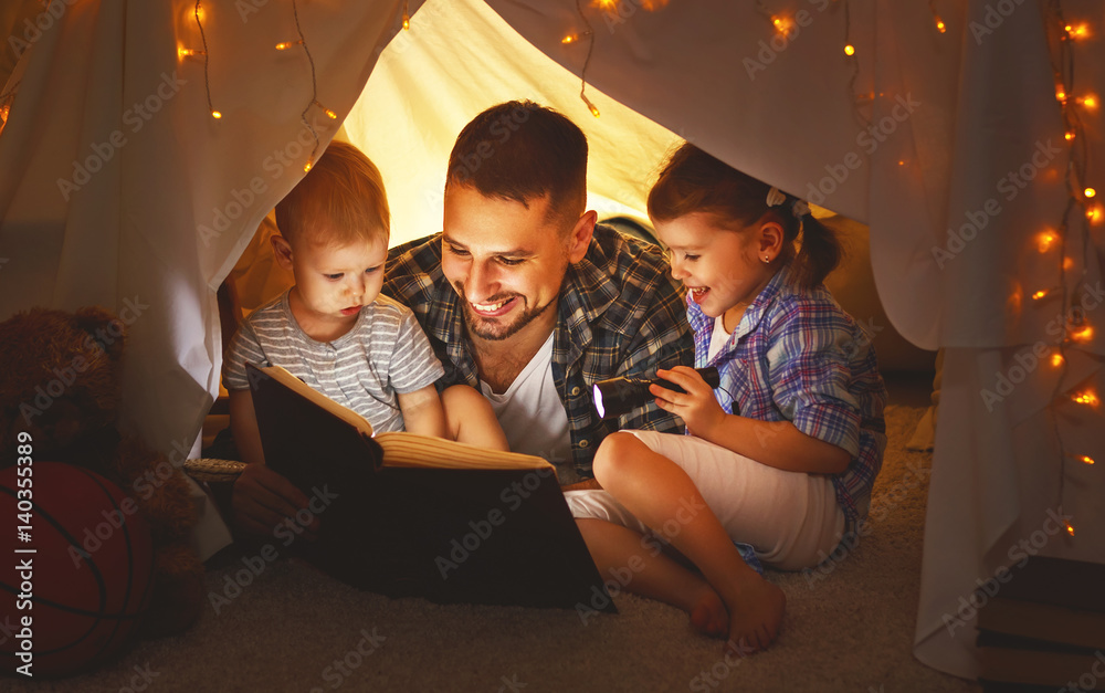 happy family father and children reading a book  in  tent at home