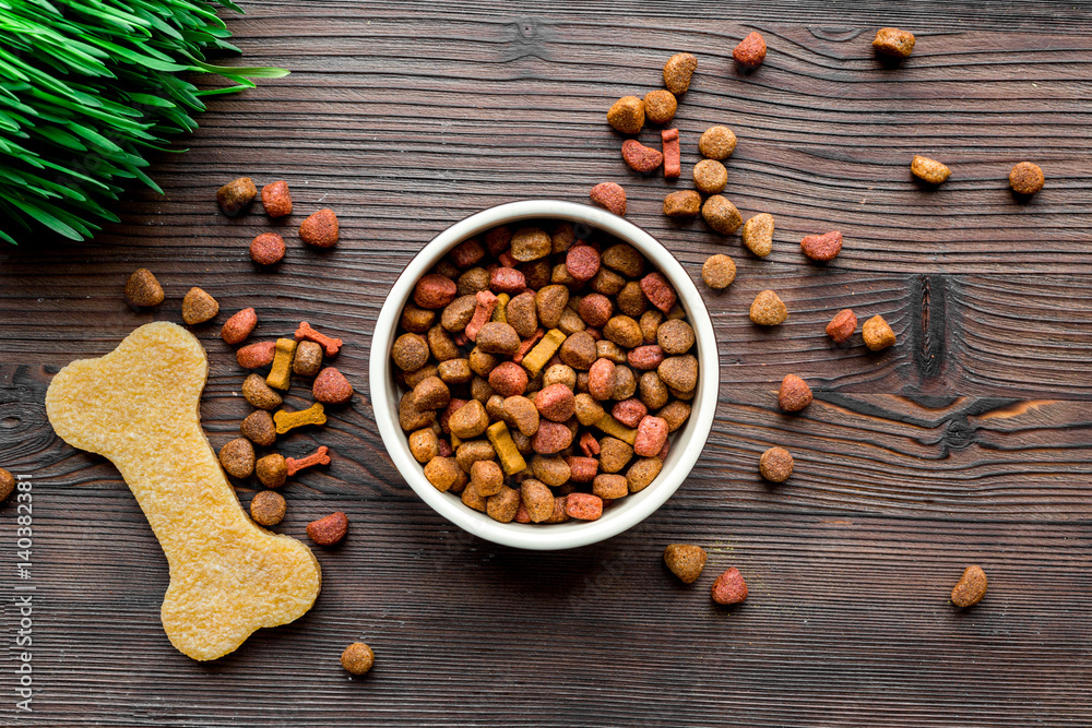 dry dog food in bowl on wooden background top view