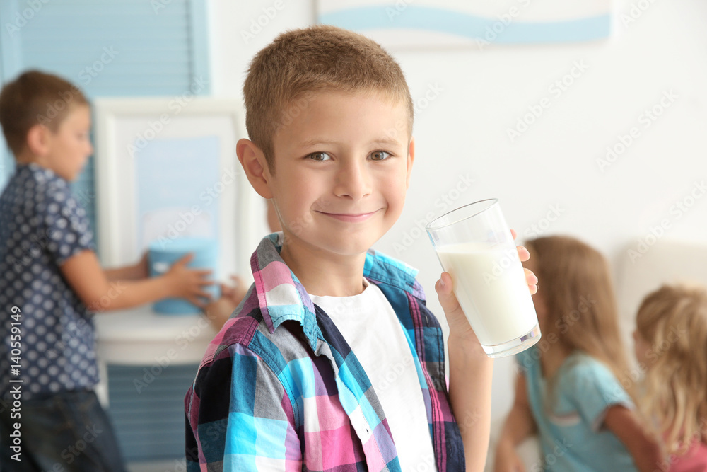 Cheerful little boy holding glass of milk and standing in the room