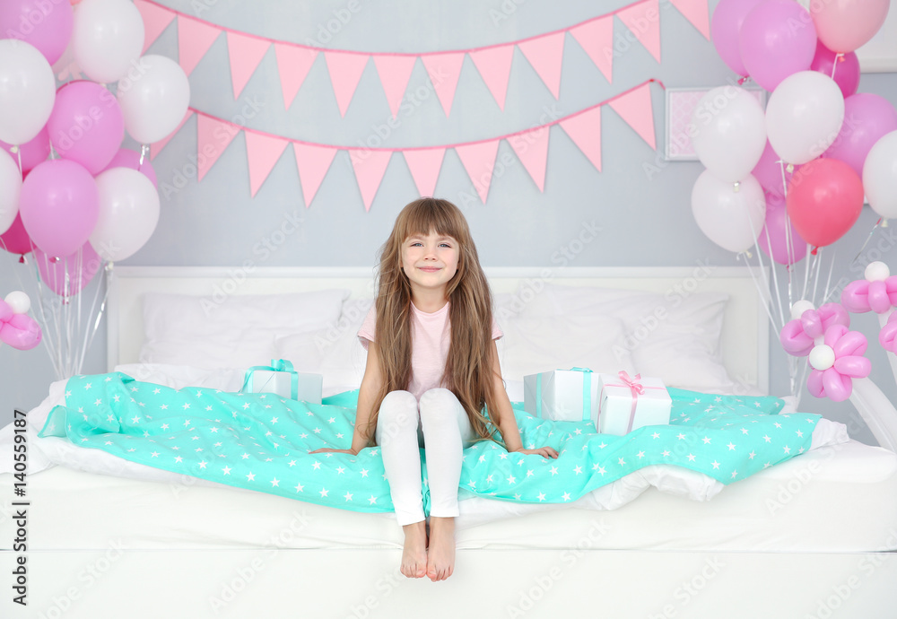 Cute girl sitting on bed in room decorated for birthday celebration