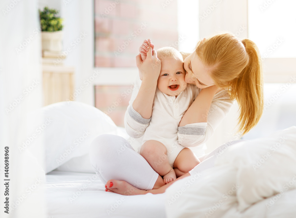 Happy family mother and baby playing, hugging  in bed