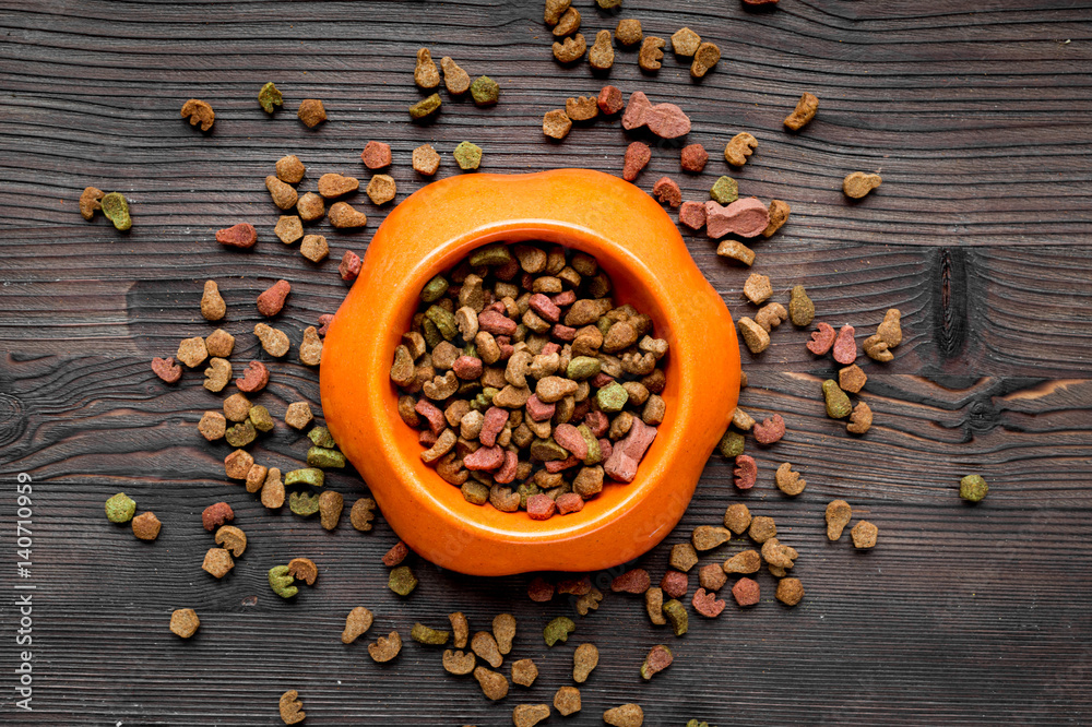 dry cat food in bowl on wooden background top view