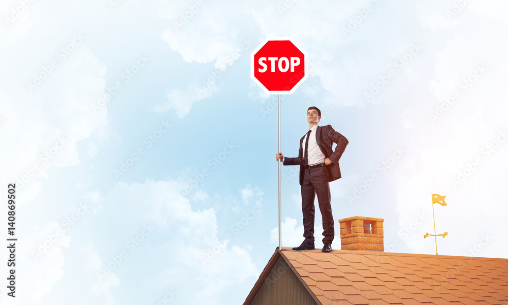 Caucasian businessman on brick house roof showing stop road sign