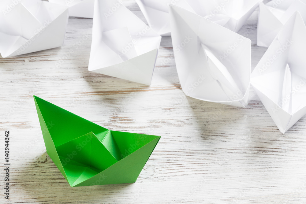 Business leadership concept with white and color paper boats on wooden table