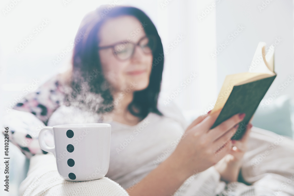 Relaxed woman drinking coffee and reading book at home