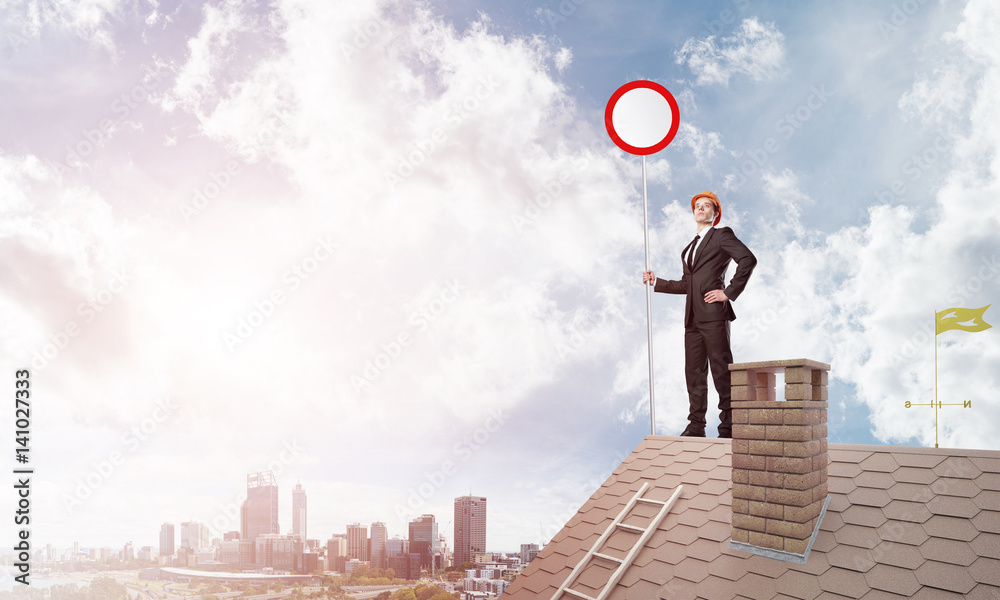 Caucasian businessman on brick house roof showing stop road sign. Mixed media