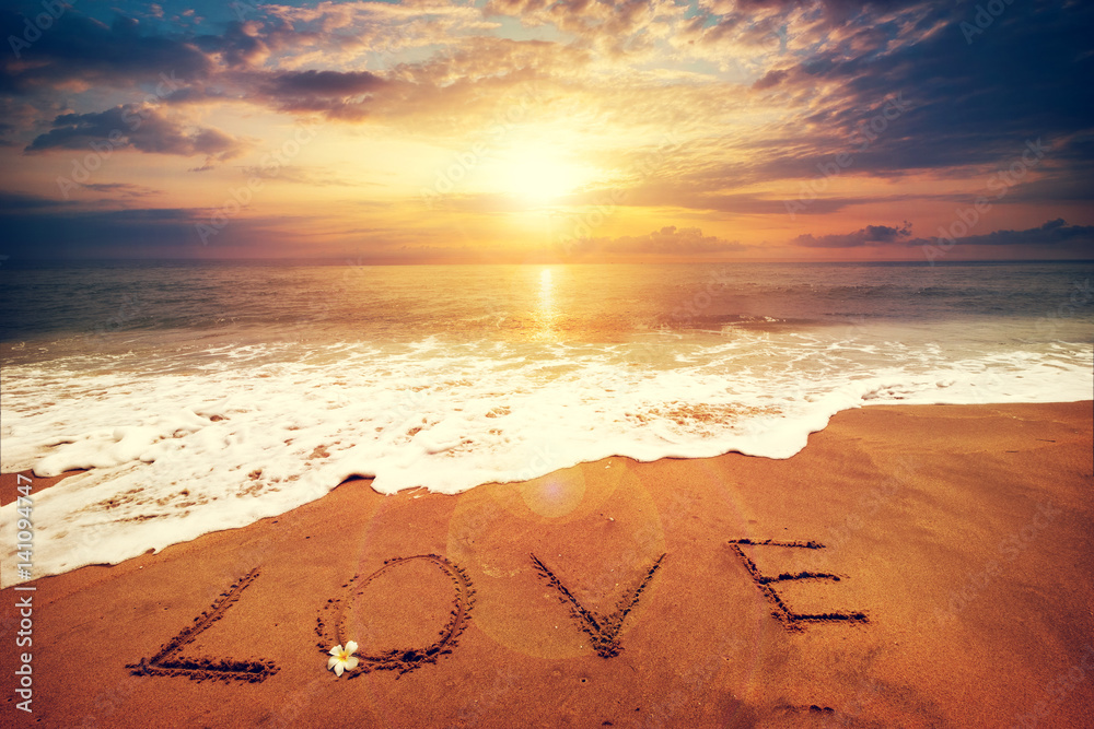 Inscription LOVE written on the sandy beach with ocean wave - sunset time. Honeymoon concept. vintag