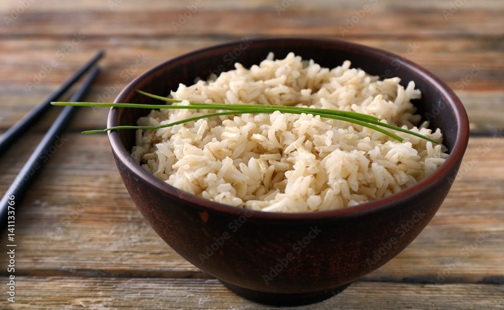 Bowl with brown rice on wooden table