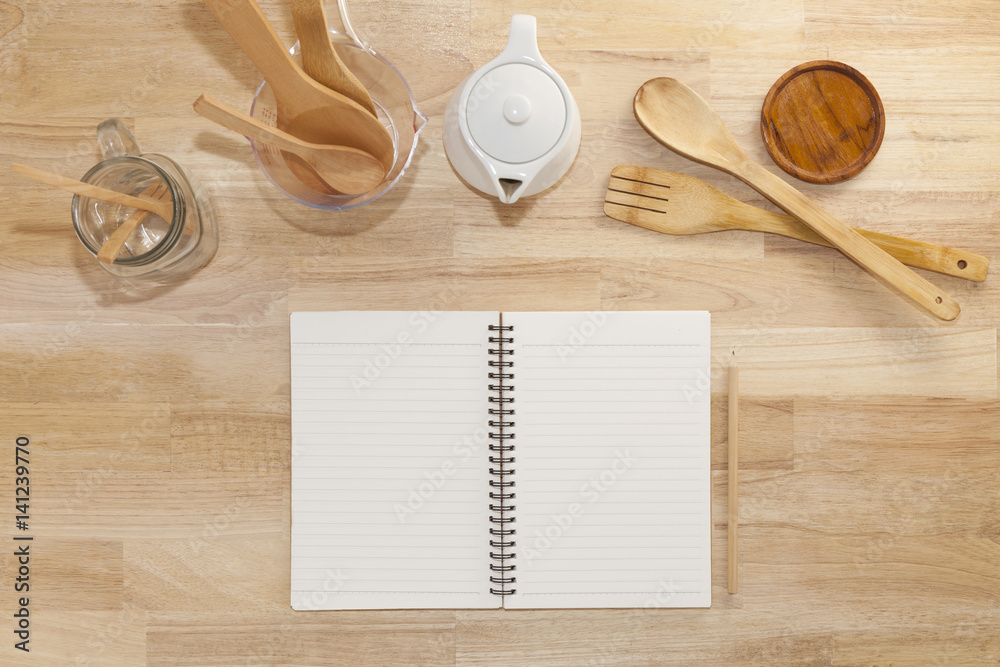 notebook with pencil,cup,glass bottle and empty measuring cup,wooden spoon on wood background.