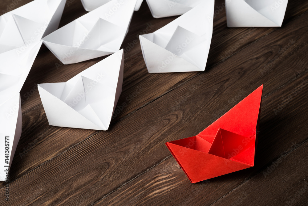 Business leadership concept with white and color paper boats on wooden table