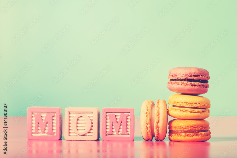 Colorful macarons with mom wood blocks on bright pastel background