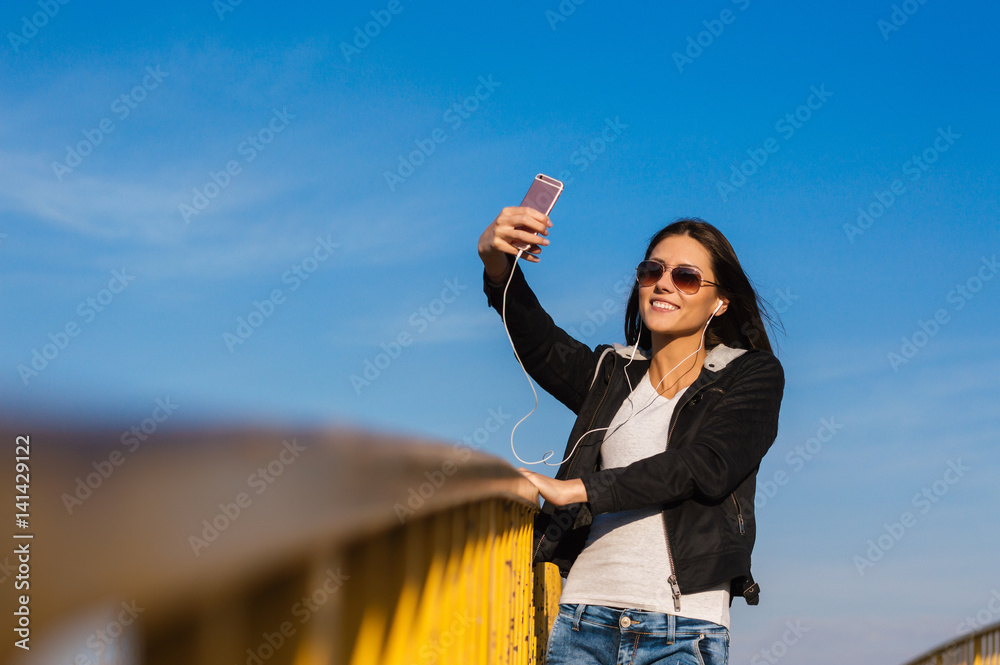 Girl making selfie on the bridge while listening to music on her mobile