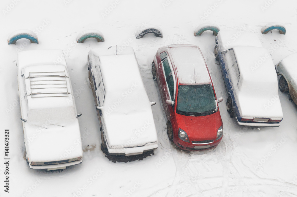 在城市院子里停车时，被雪完全覆盖的汽车被摩擦，一辆红色汽车被部分挖出