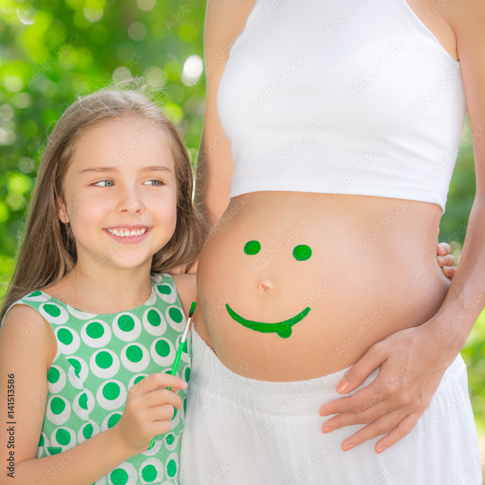 Happy child painting smile on belly of pregnant woman