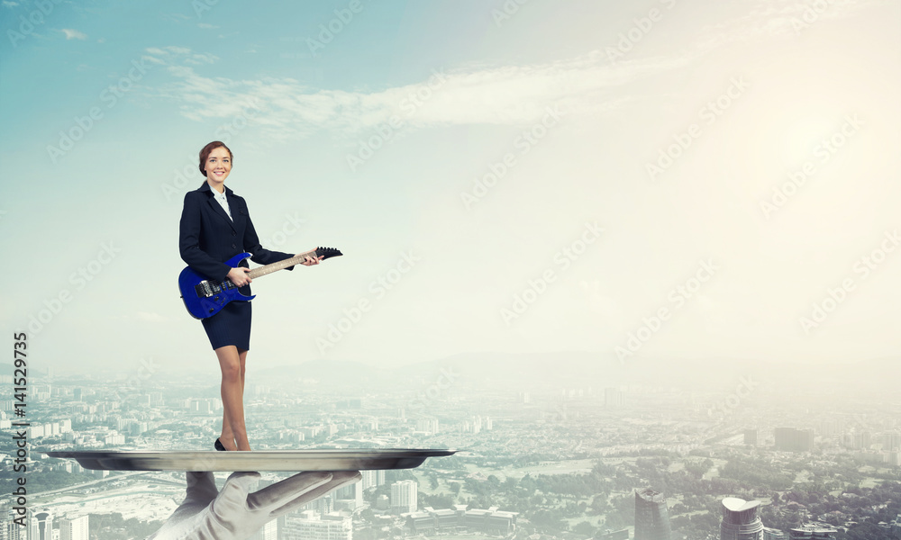 Attractive businesswoman on metal tray playing electric guitar against cityscape background