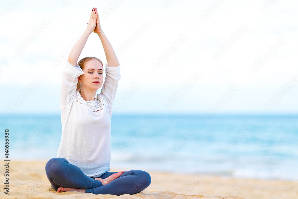 woman practices yoga and meditates in lotus position on beach