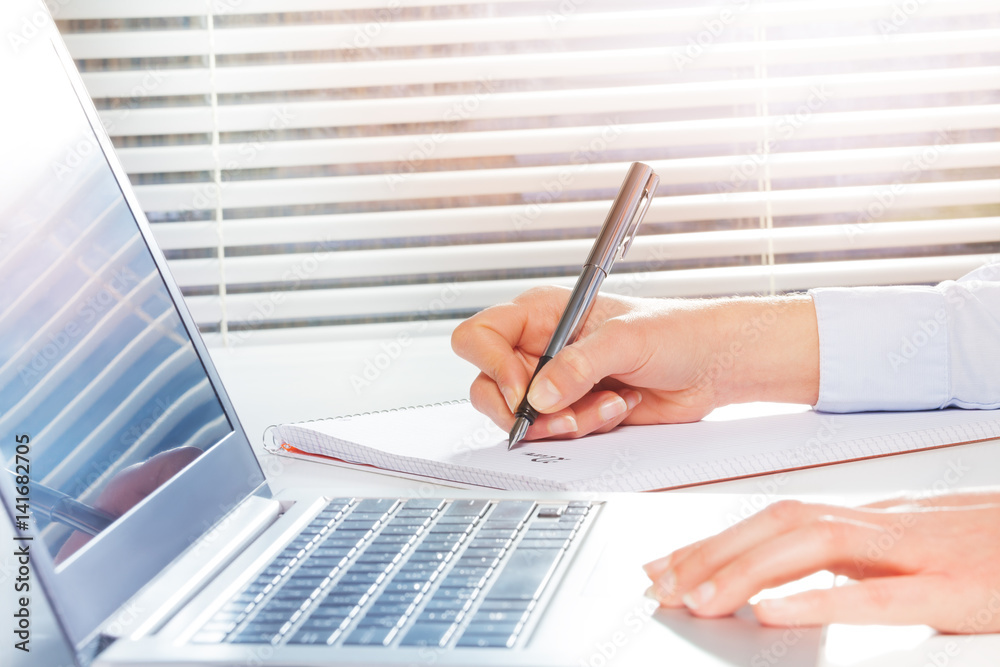 Students hands making notes next to the laptop