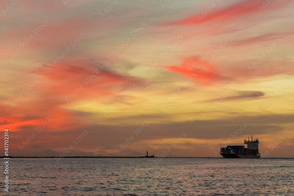 Red container ship arriving from Baltic sea at red sunset sky