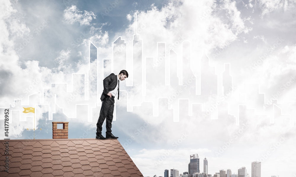 Businessman looking down from roof and modern cityscape at backg