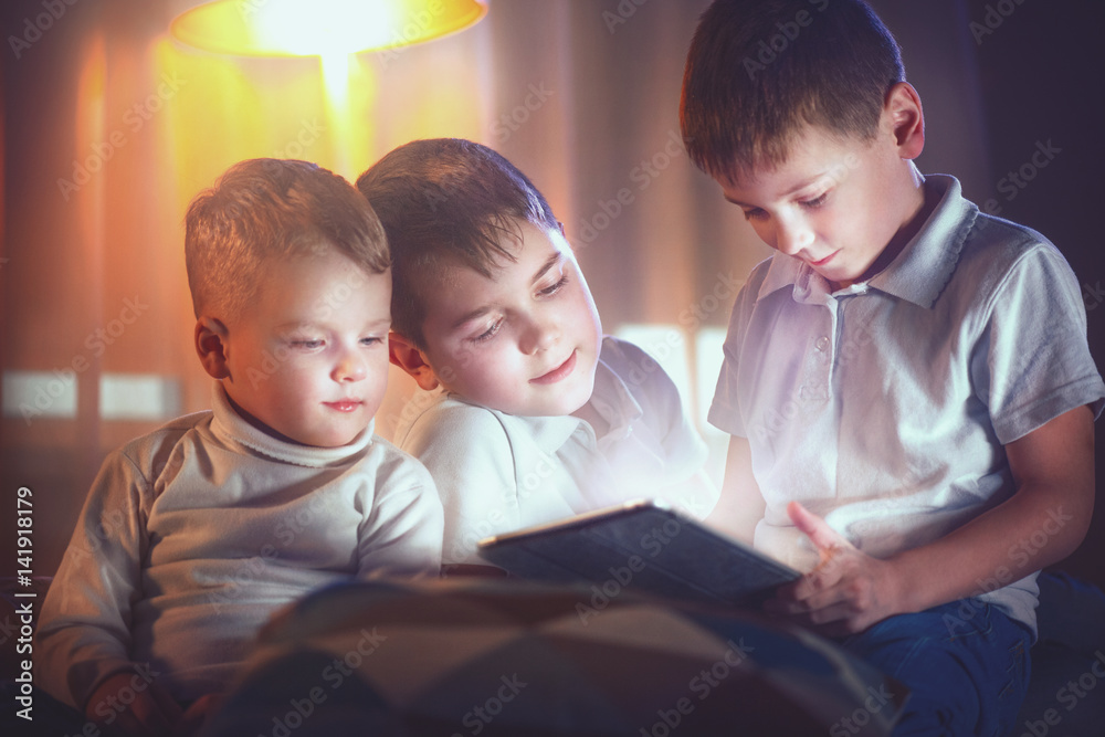 Three little boys with tablet computer in a dark room. Kids playing games on tablet pc