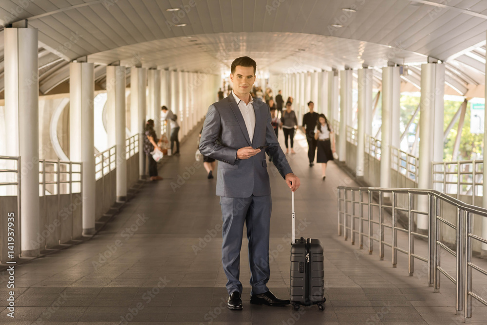 Business man with travel bag use smart phone on the walk way with crowded people in background