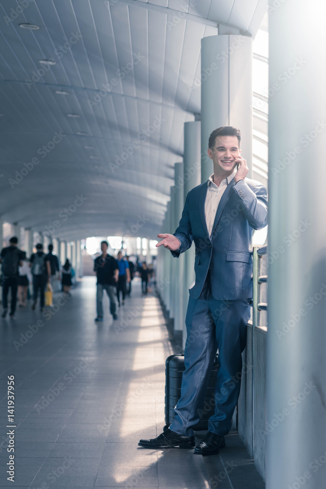 Business man with travel bag use smart phone on the walk way with crowded people in background