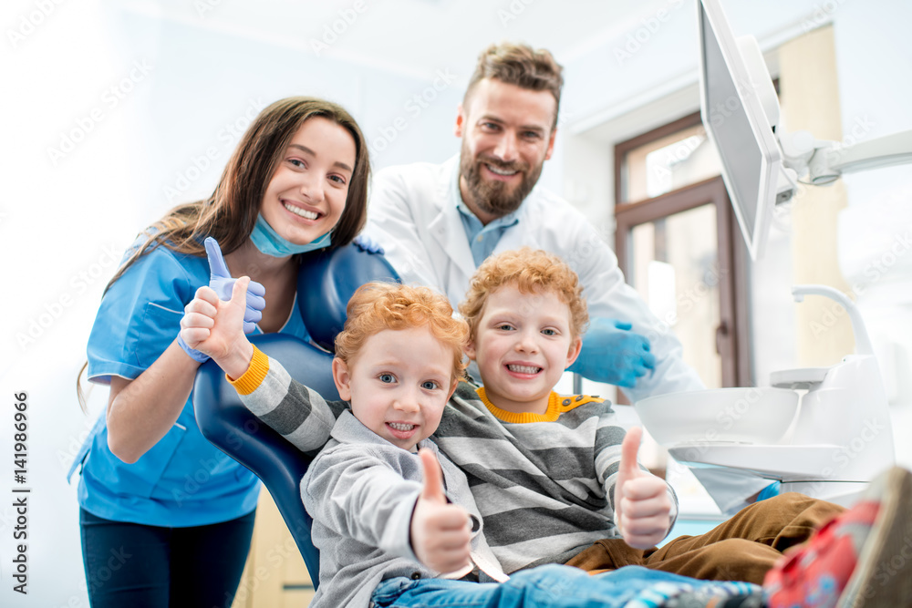 Portrait of happy young boys sitting on the chair with dentist and woman assistant at the dental off