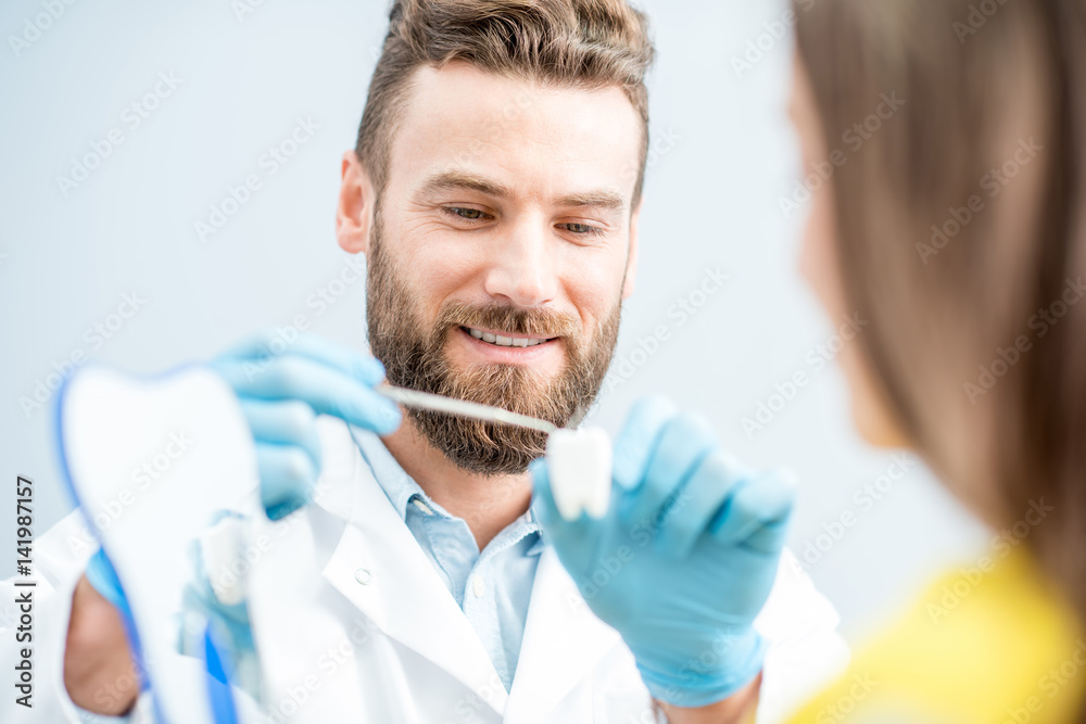 Handsome dentist consulting woman patient holding tooth model at the dental office