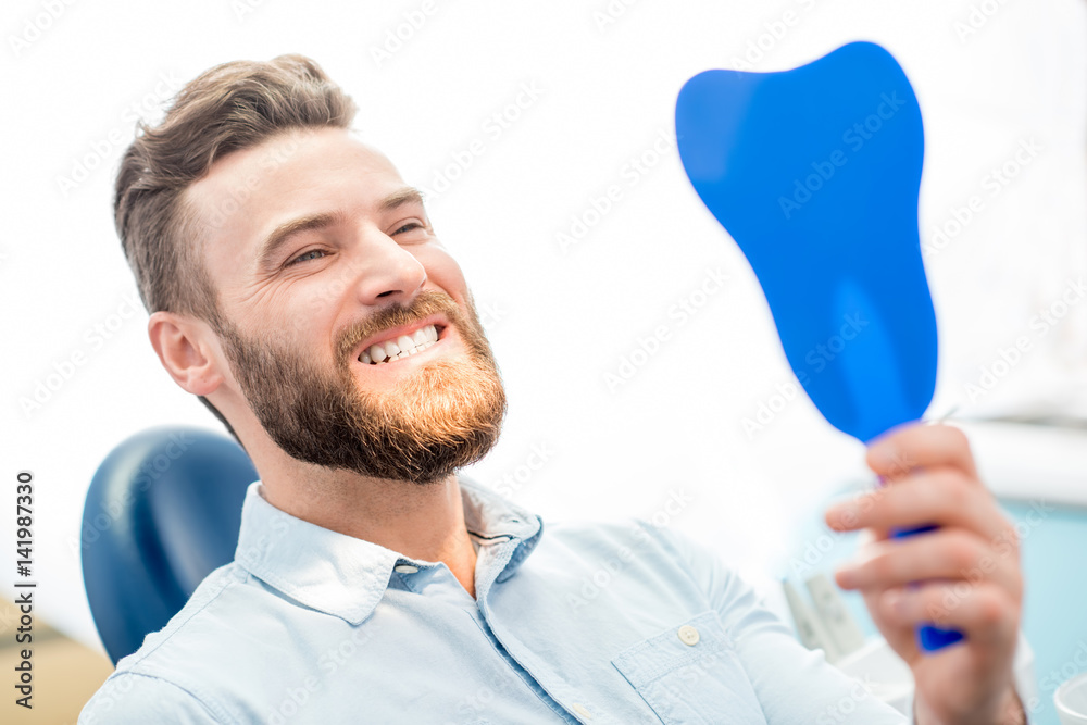 Handsome male patient looking at his beautiful smile sitting at the dental office